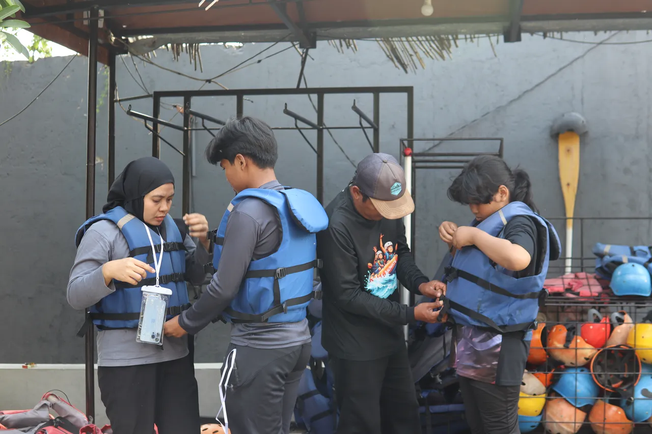 Pemandu rafting memeriksa dan memasangkan pelampung kepada peserta sebelum turun ke sungai